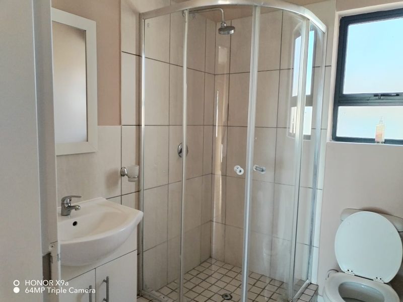 A functional bathroom featuring a corner shower enclosure, vanity basin, and toilet with neutral wall and floor tiling.