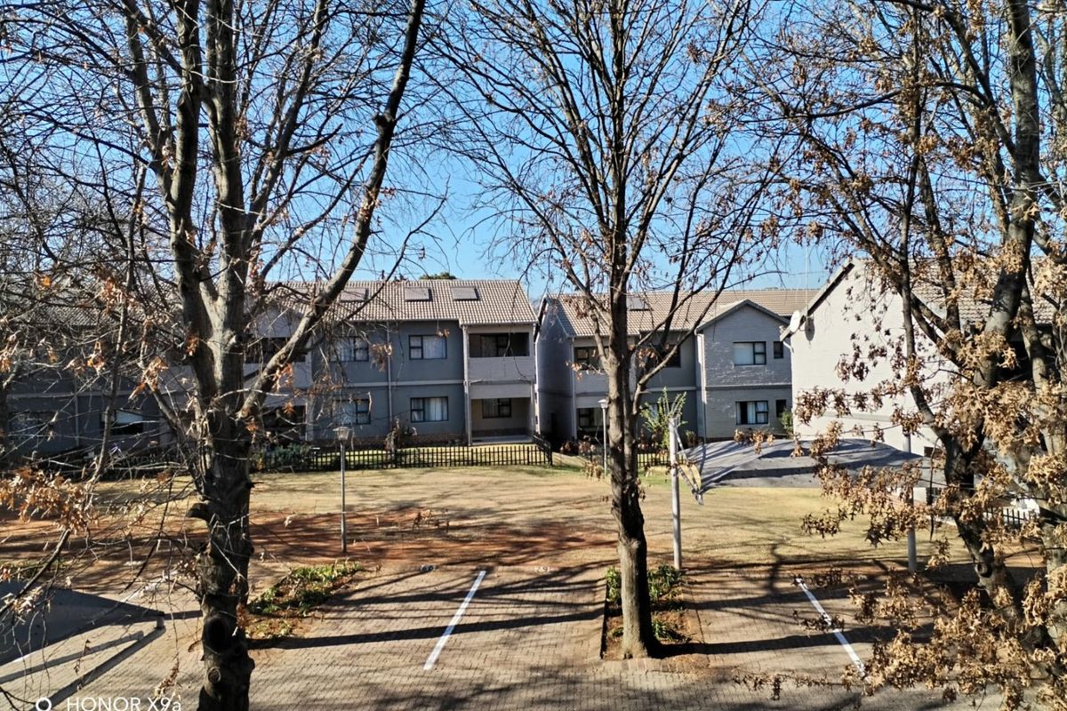 View of the apartment complex rear exterior featuring a paved parking area and communal garden space.