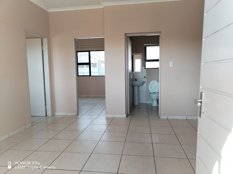 An empty living area featuring neutral wall tones and ceramic floor tiles, with direct access to an adjacent bedroom and a functional bathroom.