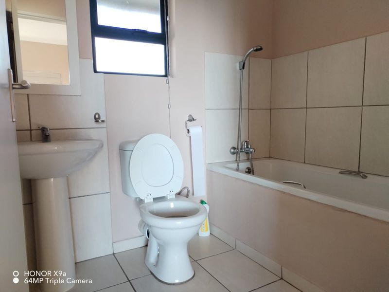 A functional bathroom featuring a pedestal basin, toilet, and a bathtub with a shower mixer, finished with neutral wall and floor tiles.