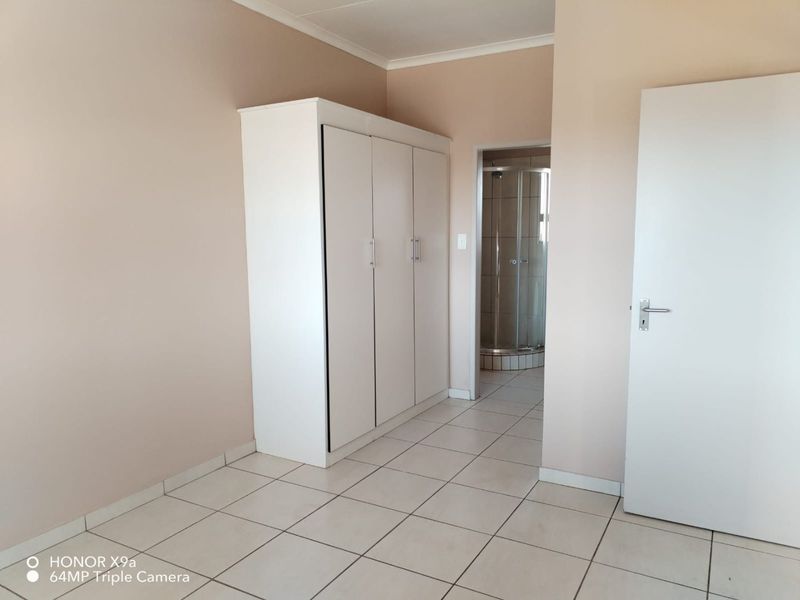 A clean, empty bedroom featuring tiled flooring, a built-in wardrobe, and direct access to an en-suite bathroom.
