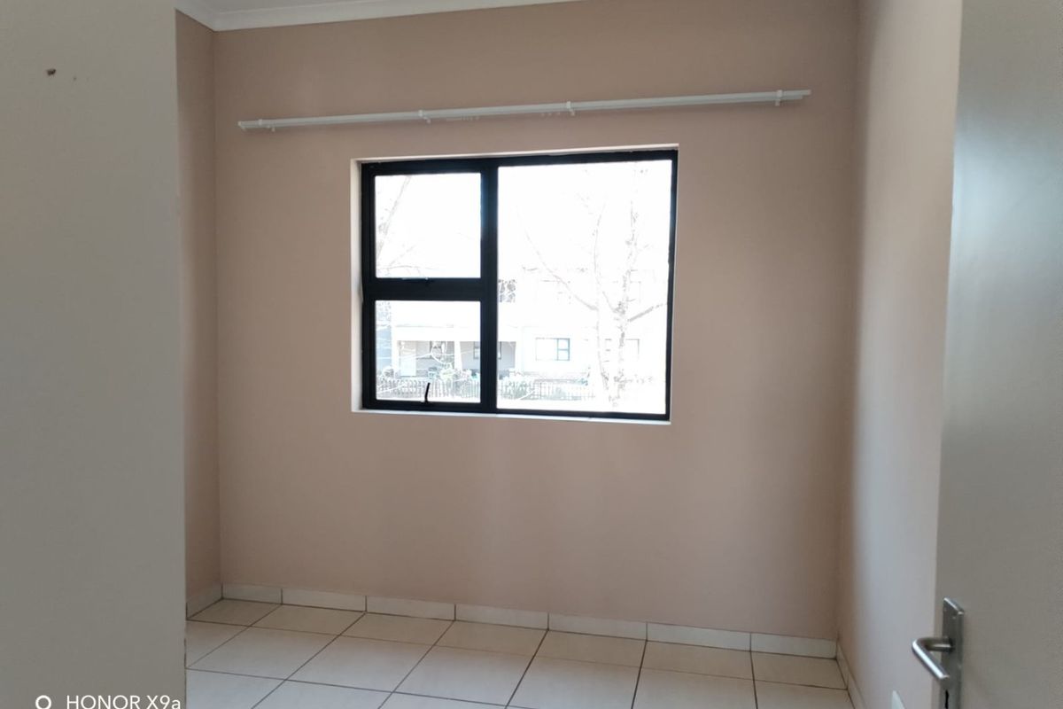 An empty bedroom featuring neutral wall paint, tiled flooring, and a black aluminium window frame with an installed curtain rod.