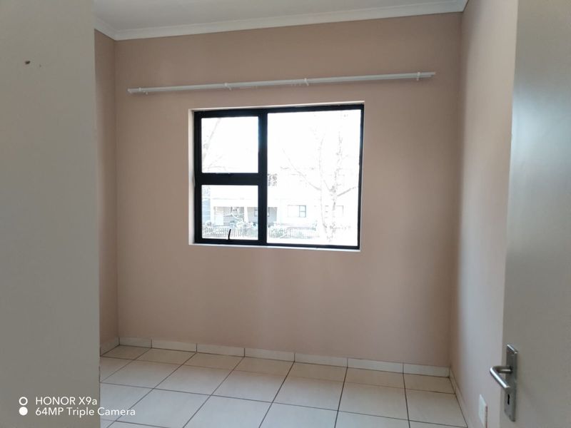 An empty bedroom featuring neutral wall paint, tiled flooring, and a black aluminium window frame with an installed curtain rod.