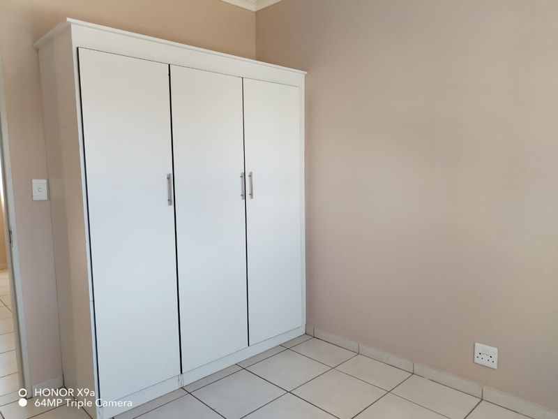 A clean, empty bedroom featuring neutral wall tones, white tiled flooring, and a modern built-in wardrobe with silver handles.