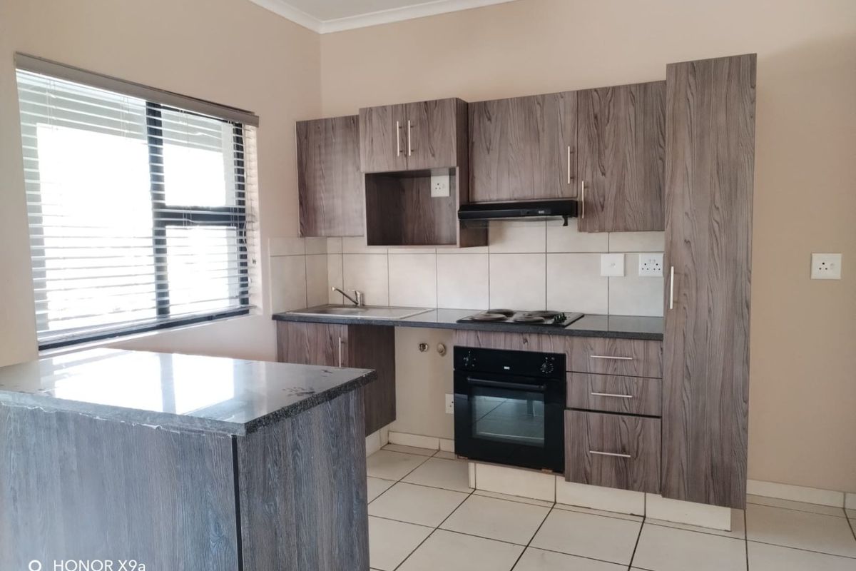 Modern kitchen featuring wood-grain cabinetry, granite countertops, built-in oven, electric hob, extractor fan, and tiled flooring.