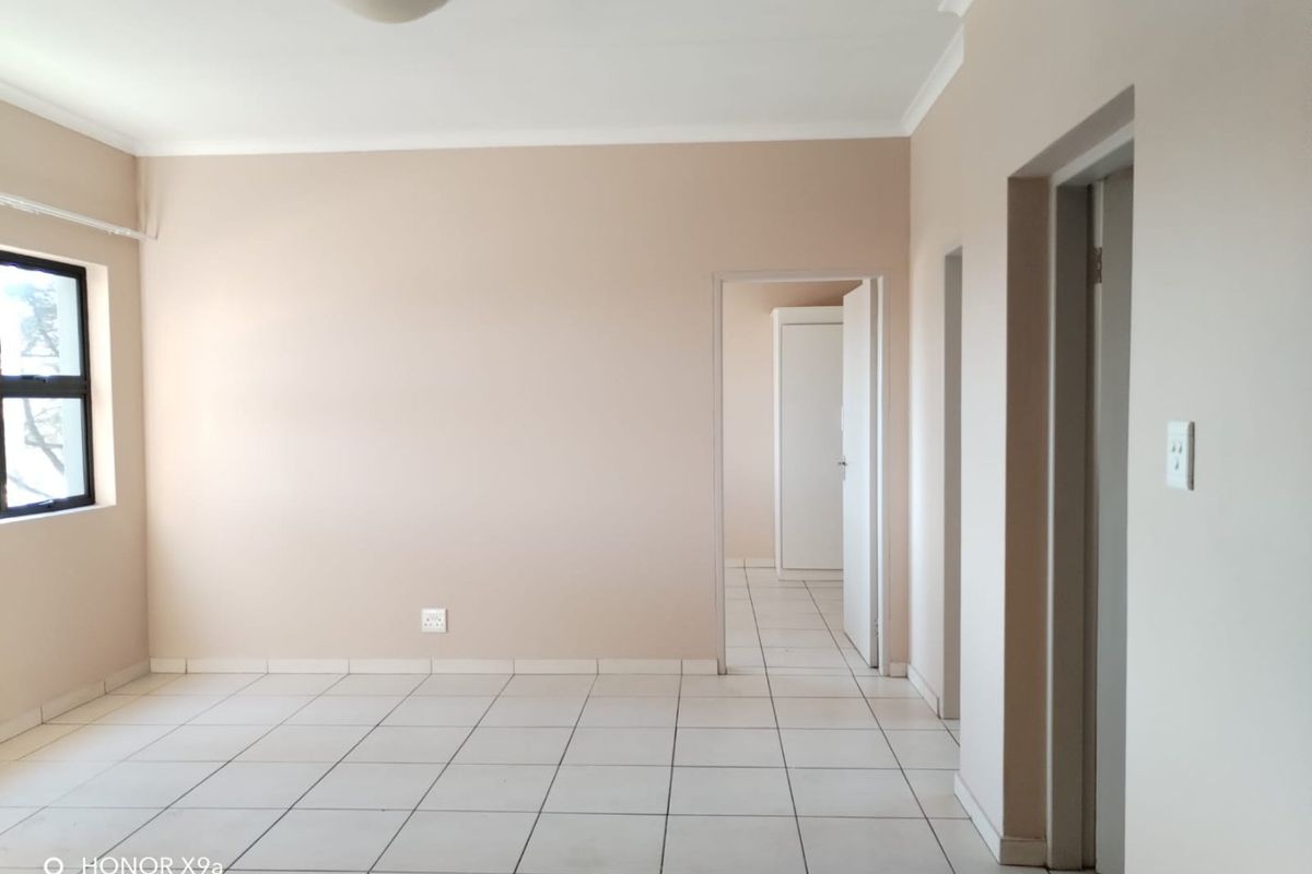 A bright, empty living area featuring neutral walls, tiled flooring, and multiple doorways leading to other parts of the apartment.