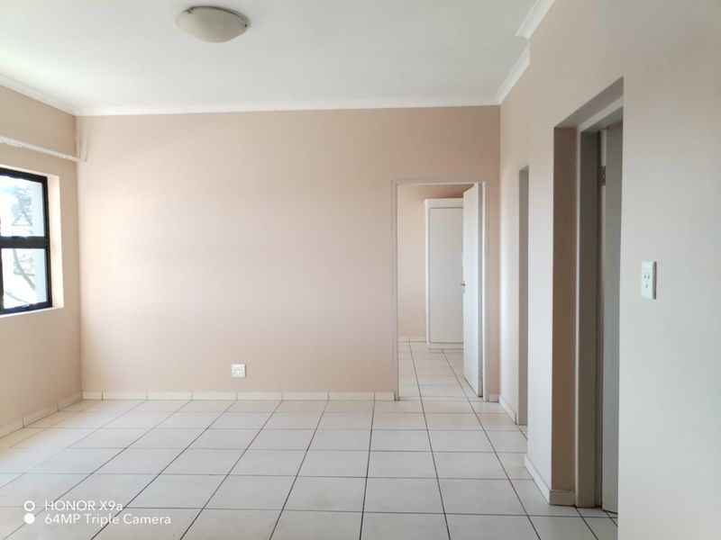 A bright, empty living area featuring neutral walls, tiled flooring, and multiple doorways leading to other parts of the apartment.
