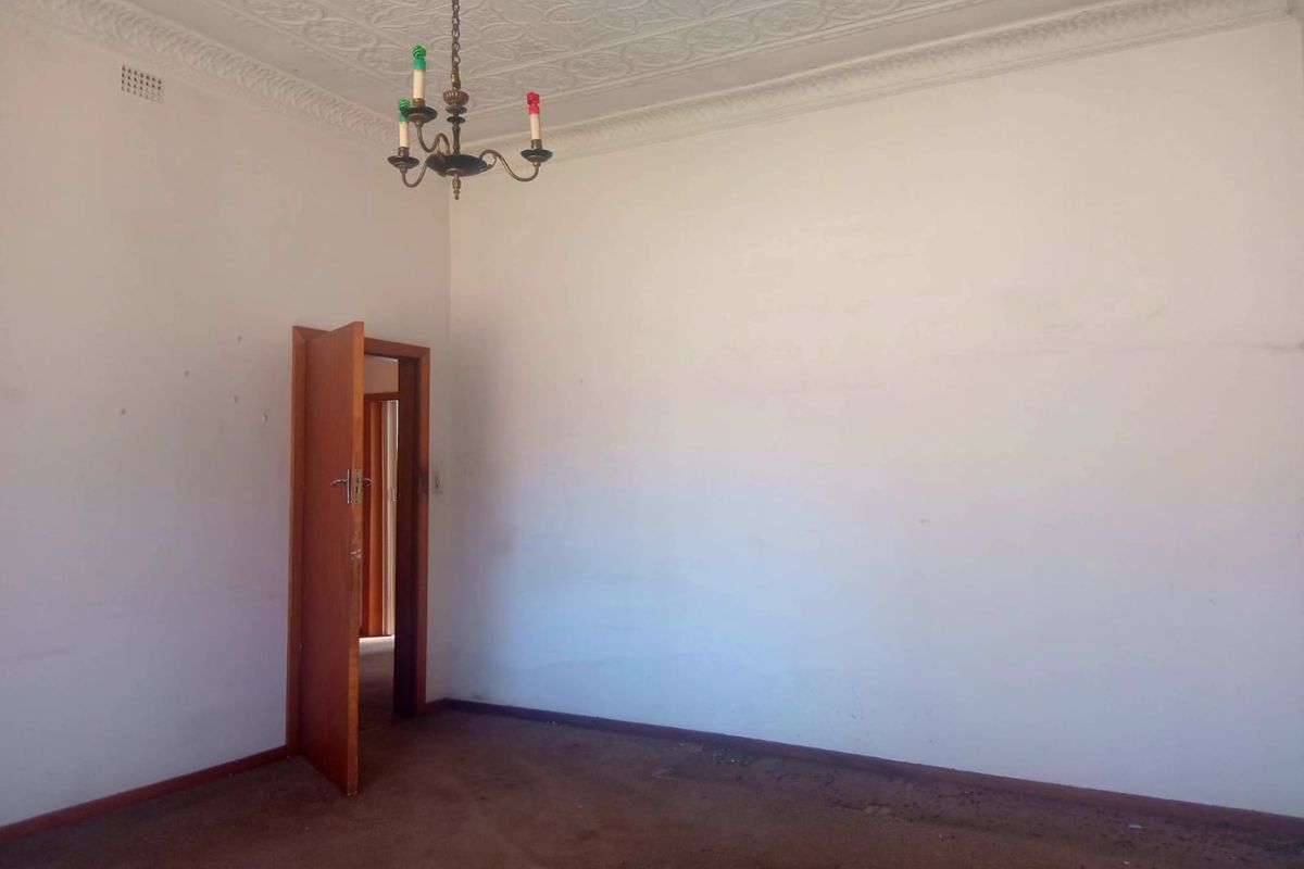 An empty bedroom featuring an ornate plaster ceiling, coving, and a vintage chandelier, awaiting renovation to refresh the worn carpet and wall finishes.