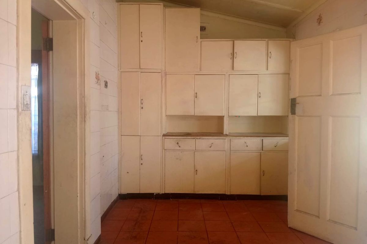 A dated kitchen area featuring original built-in cabinetry, tiled walls, and terracotta-style floor tiles, offering significant potential for renovation and modernization.