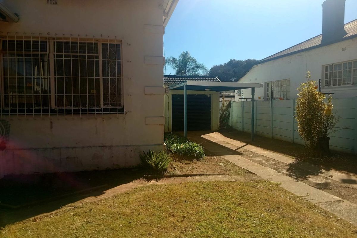 Rear exterior view showing a carport, concrete driveway, and perimeter wall with electric fencing, set against the side of the main dwelling.