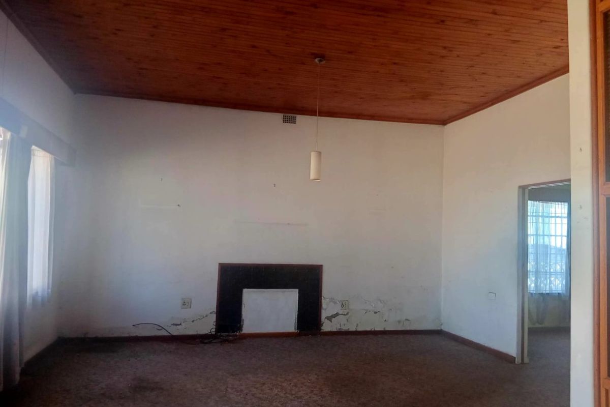 Spacious living room featuring a fireplace, timber ceiling, and carpet flooring, requiring cosmetic updates and wall repairs.