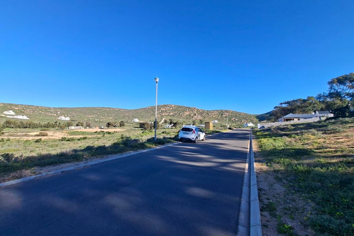 A view of the paved residential street and surrounding landscape, showcasing the access and setting of the vacant land.