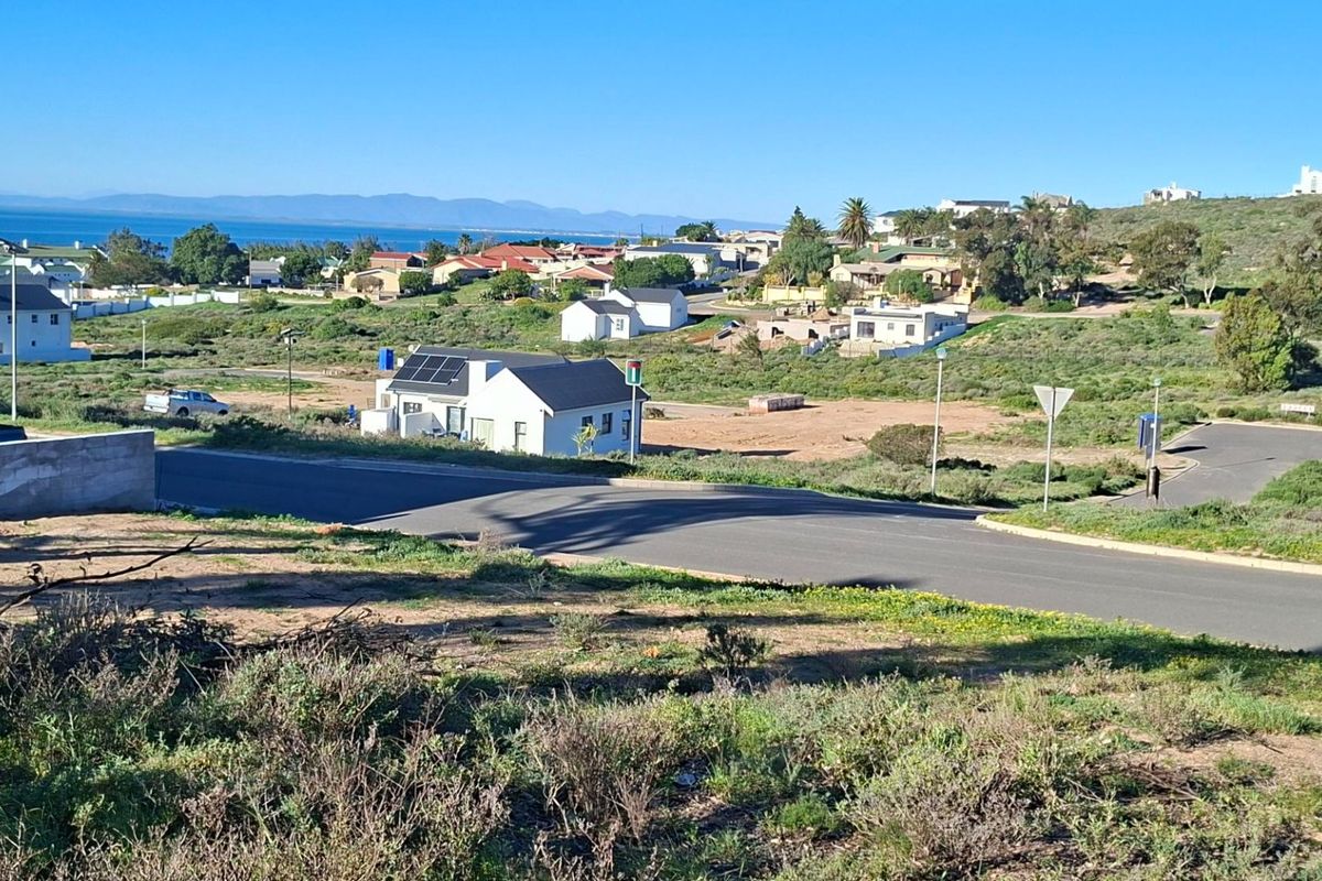 An elevated view of a residential area featuring paved roads, surrounding coastal landscape, and distant ocean views.
