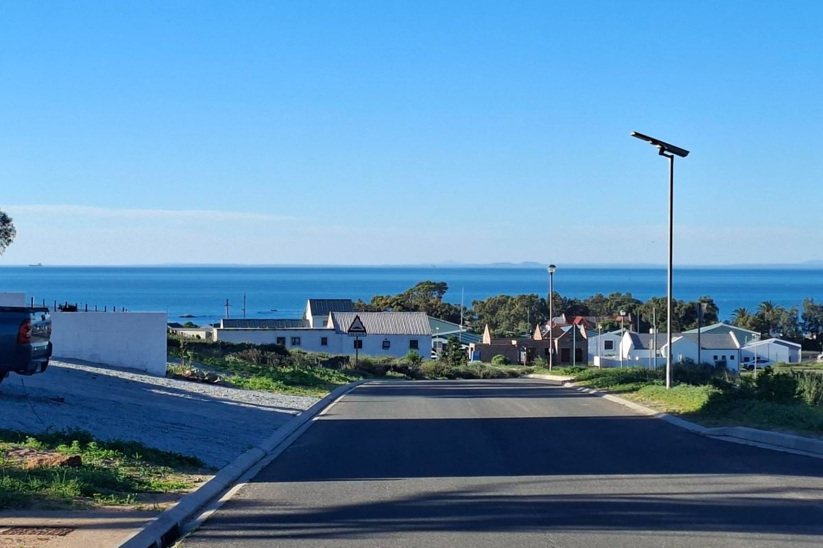A clear street view showing the paved road, solar street lighting, and a scenic coastal outlook in the distance.