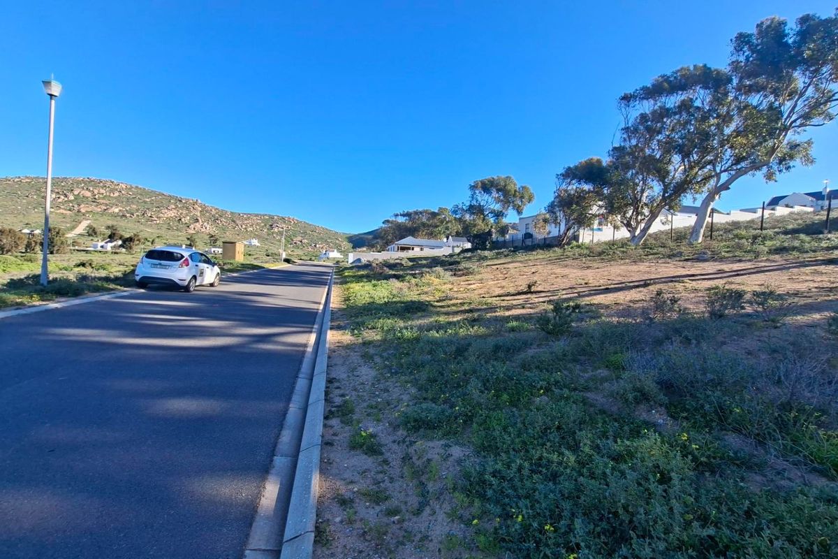 A view of the paved street and kerbing adjacent to the vacant residential land, featuring established trees and surrounding hillside landscape.