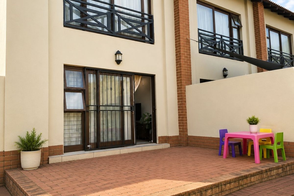A well-maintained rear townhouse exterior featuring a paved patio, sliding glass doors with security gates, and upper-level balconies with metal railings.