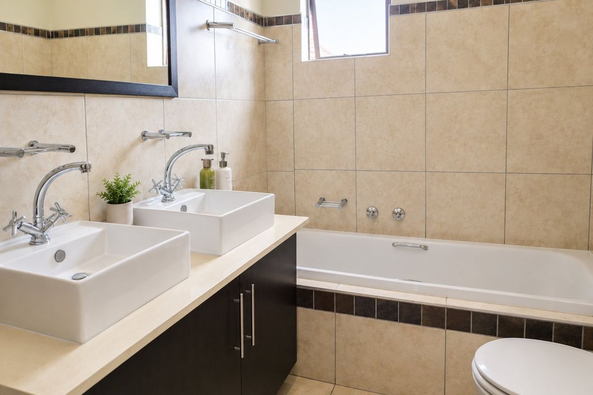 A well-maintained bathroom featuring a double vanity with vessel sinks, a built-in bathtub, and neutral wall tiling with decorative accents.