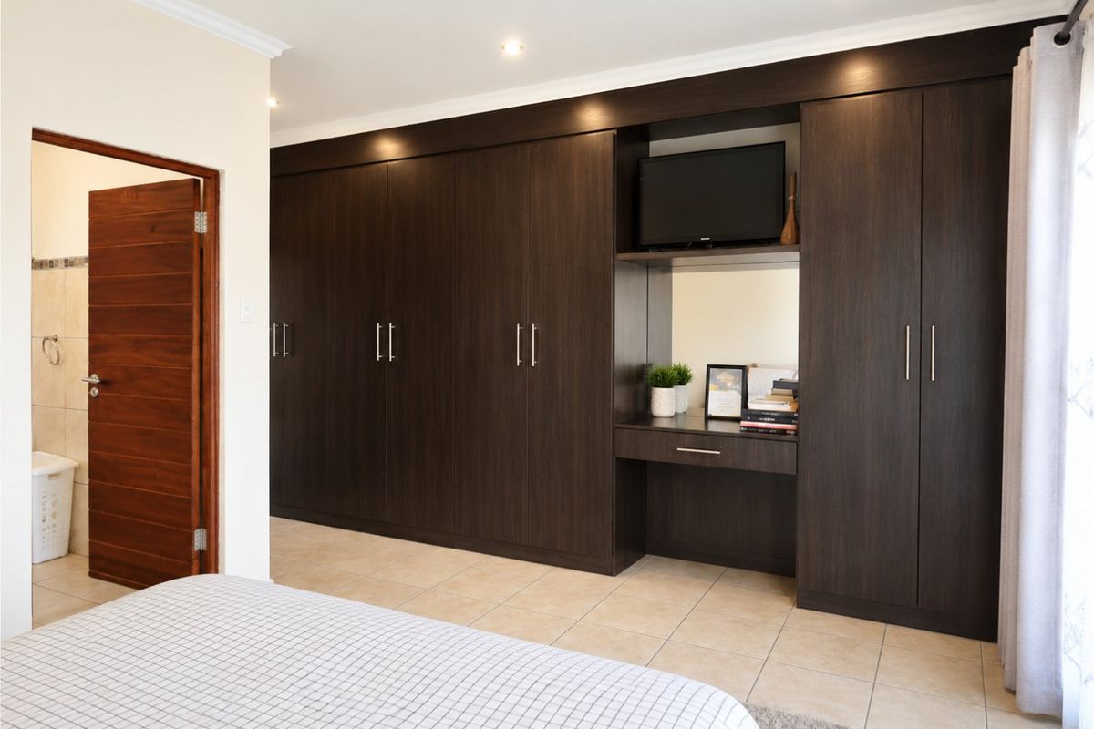 A well-maintained bedroom featuring extensive dark wood built-in cabinetry with an integrated vanity unit, tiled flooring, and direct access to an en-suite bathroom.