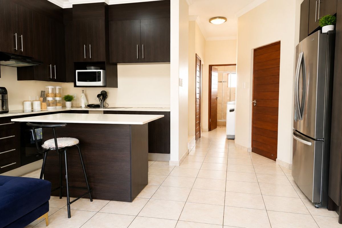 Modern kitchen featuring dark wood cabinetry, stone countertops, and a breakfast nook, leading into a tiled hallway with access to additional rooms.