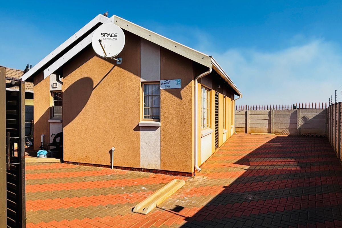 Rear exterior view of the house featuring paved ground, precast boundary walls with electric fencing, and a satellite dish mounted on the facade.
