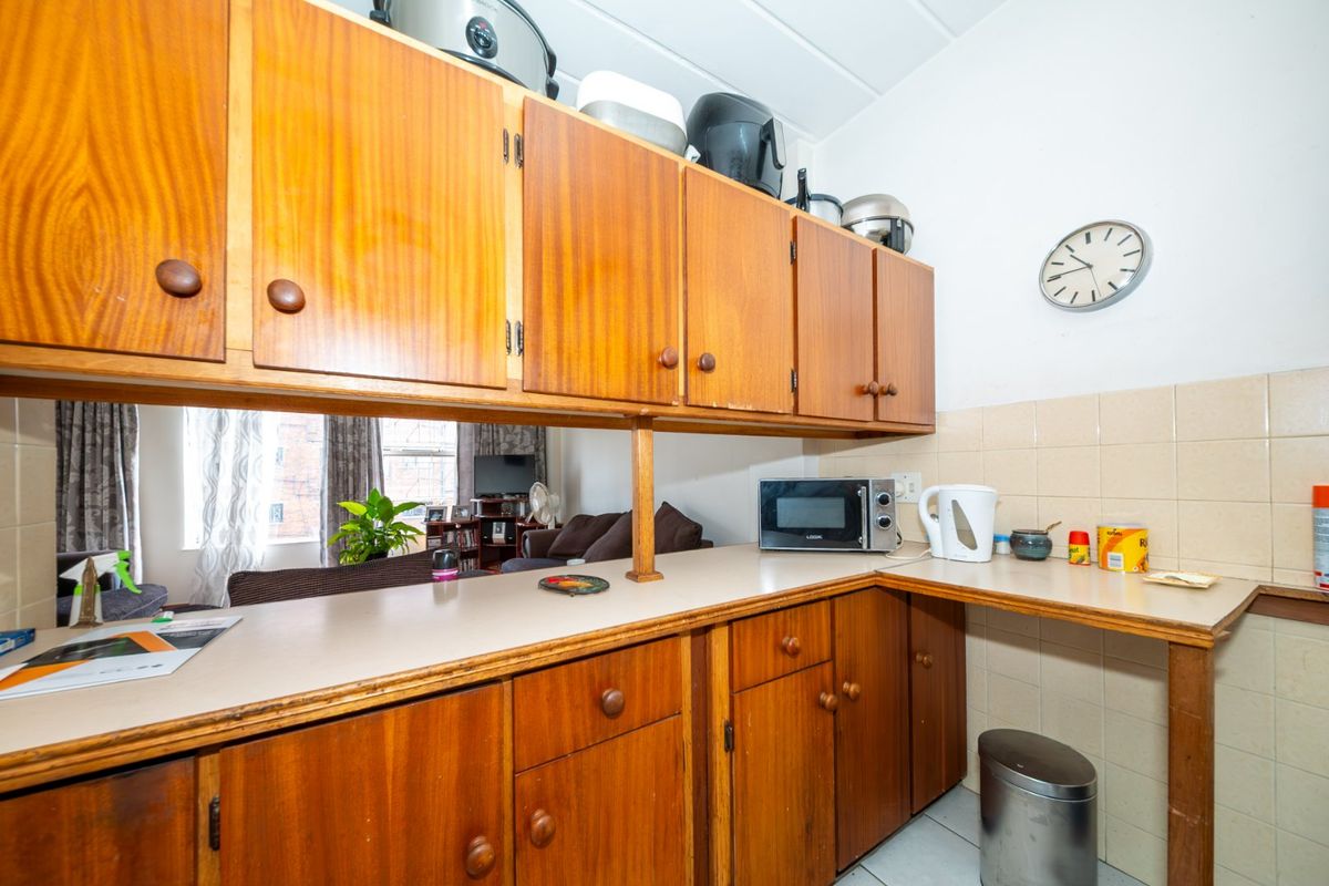 A dated kitchen area featuring wooden cabinetry, laminate countertops, and a tiled backsplash, offering a functional layout with potential for modern renovation.