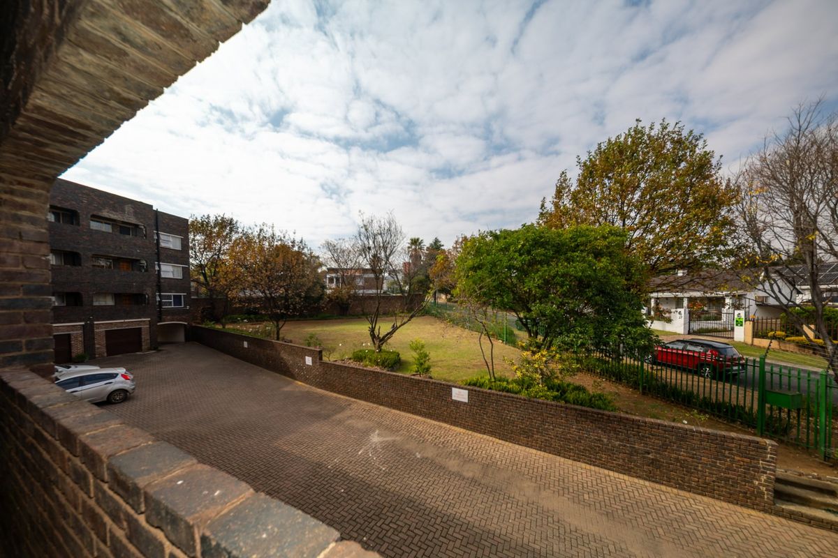 An elevated view of the apartment complex rear area, featuring paved parking, a brick boundary wall, and a shared garden space.