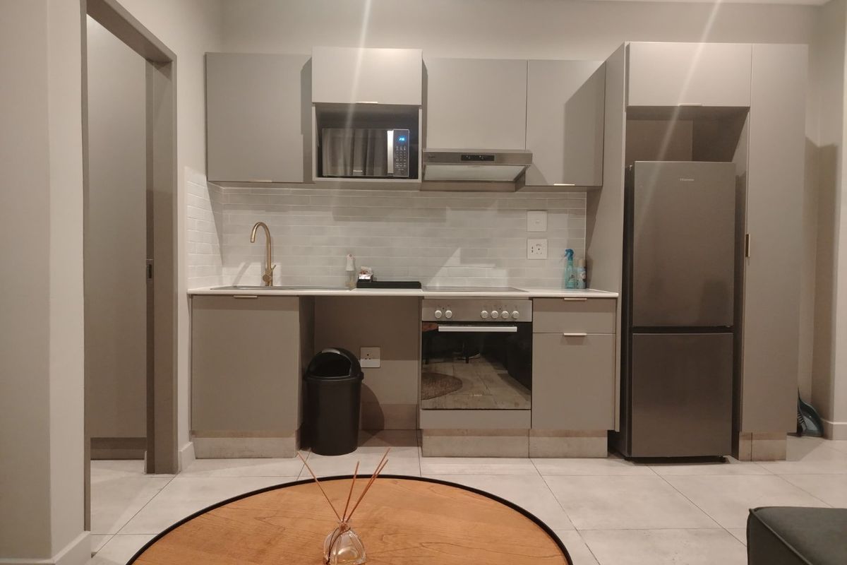 Modern open-plan kitchen featuring sleek grey cabinetry, subway tile backsplash, stone countertops, and integrated appliances including an oven and extractor fan.