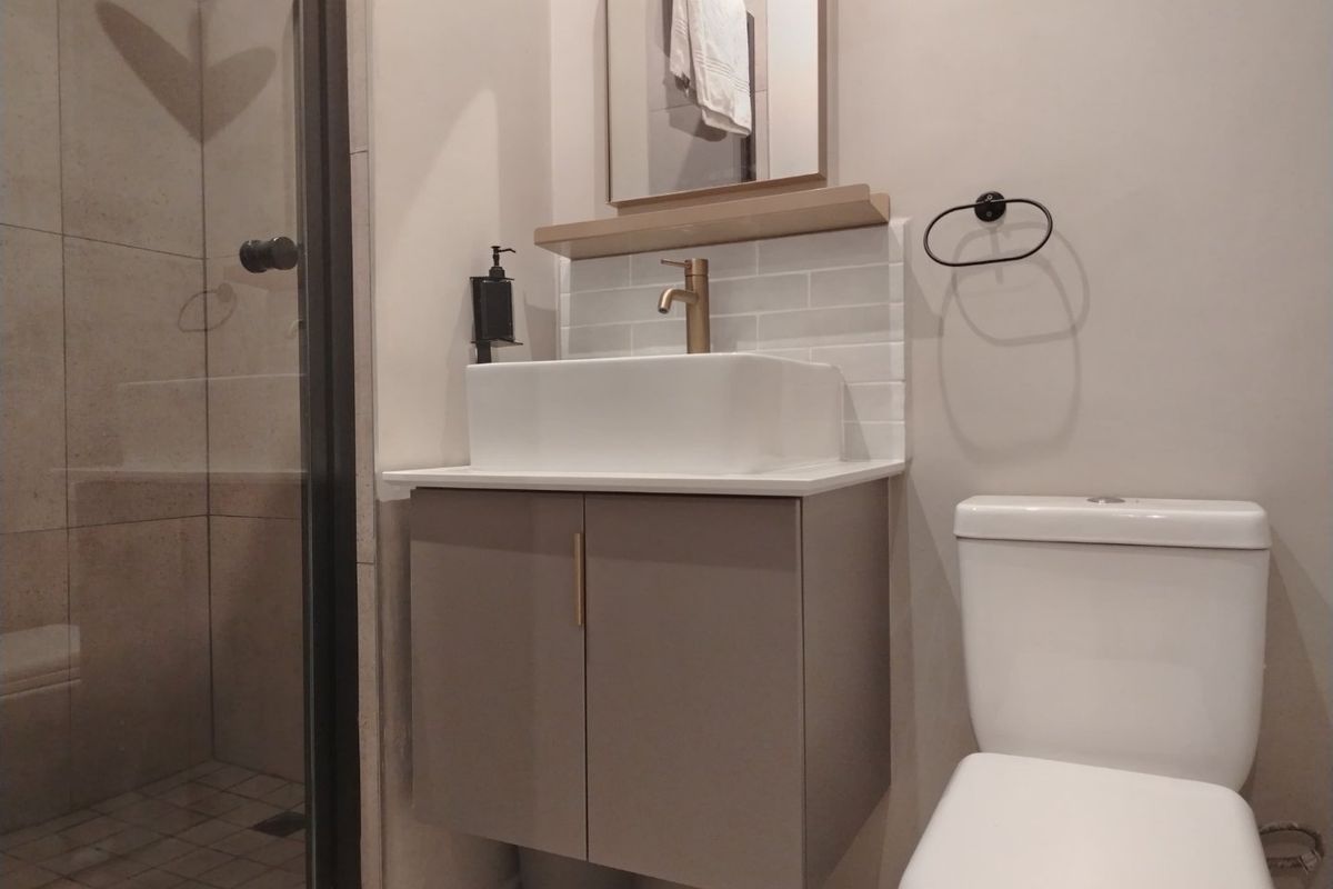 Modern bathroom featuring a floating vanity with a vessel sink, brass faucet, subway tile backsplash, and a glass-enclosed shower.