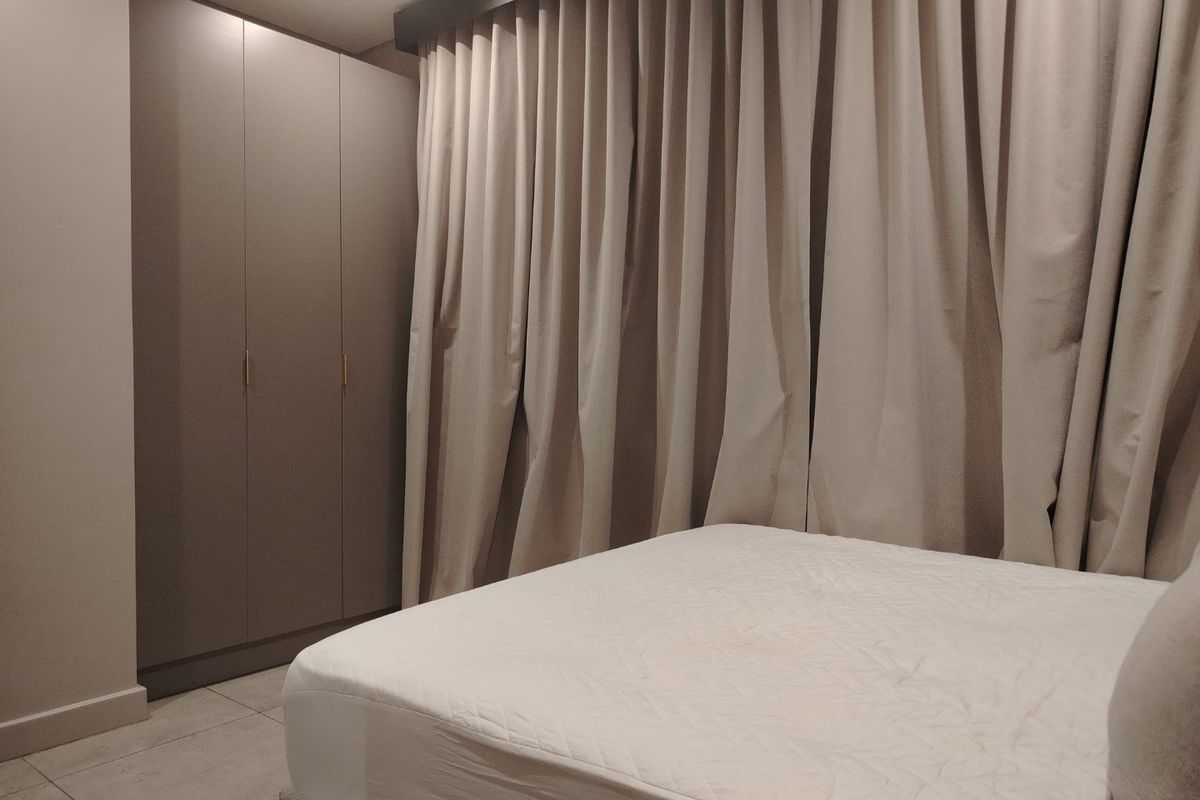 A modern bedroom featuring neutral-toned built-in wardrobes, tiled flooring, and floor-to-ceiling curtains, creating a clean and contemporary living space.