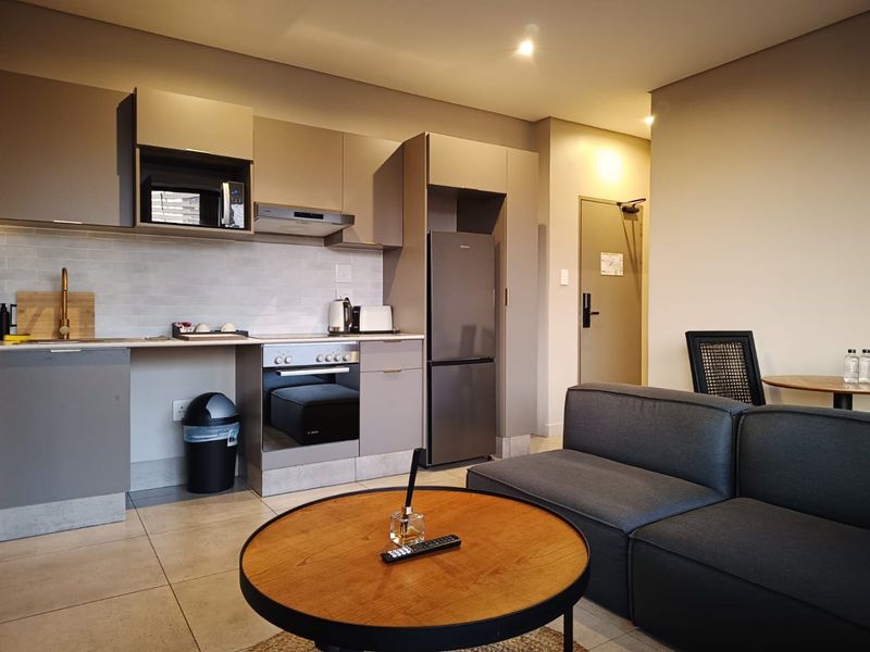 Modern open-plan apartment featuring a sleek kitchen with built-in appliances, tiled flooring, and recessed lighting, seamlessly flowing into the living area.
