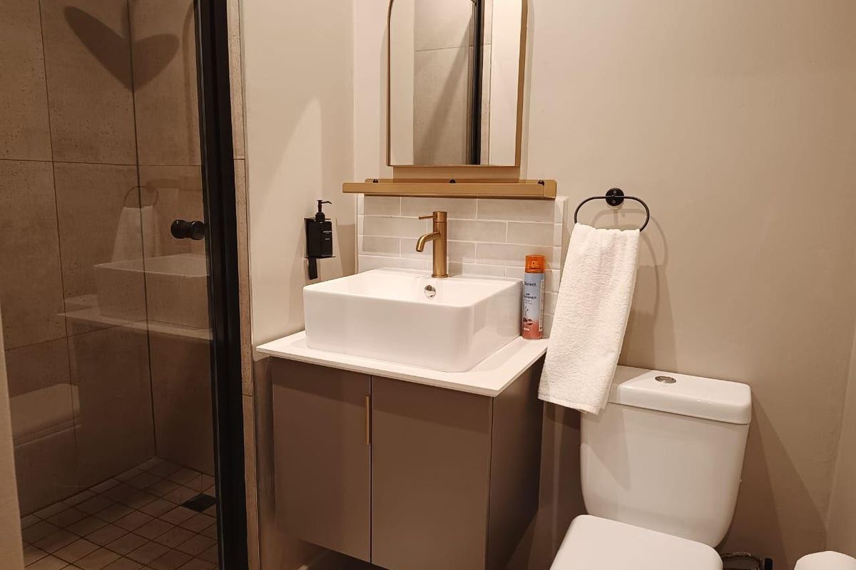 Modern bathroom featuring a vessel sink on a wall-mounted vanity, brass fixtures, arched mirror, and a glass-enclosed shower with tiled finishes.