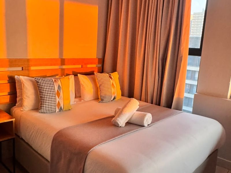 A well-maintained bedroom featuring tiled flooring, a wall-mounted split-system air conditioner, and large windows with full-length curtains.