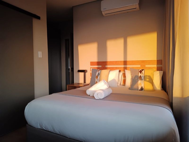 A well-maintained bedroom featuring a timber headboard, wall-mounted air conditioning unit, and a sliding door, bathed in warm natural light.