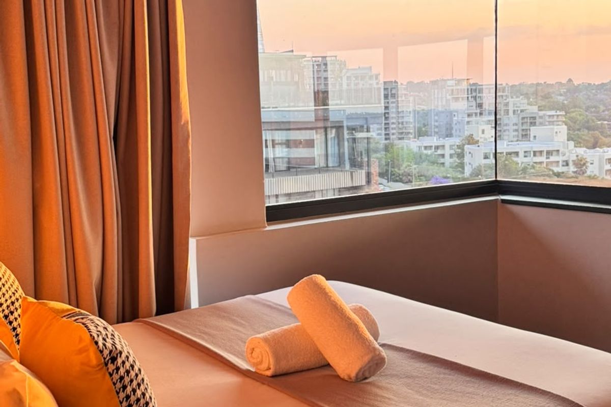 A well-lit bedroom featuring a large corner window that offers expansive city views and natural light.