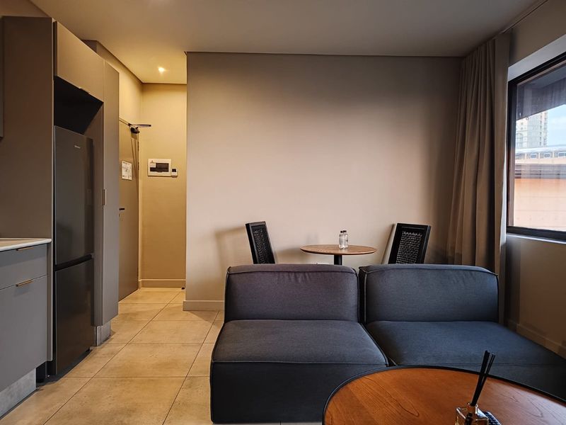 A modern open-plan living area featuring neutral tiled flooring, built-in kitchen cabinetry, and recessed lighting, creating a clean and functional living space.
