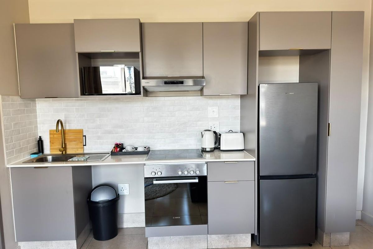Modern kitchen featuring sleek grey cabinetry, stone countertops, subway tile backsplash, and integrated appliances including an oven, hob, and microwave.