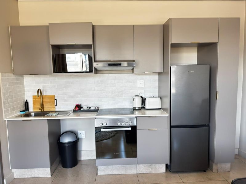 Modern kitchen featuring sleek grey cabinetry, stone countertops, subway tile backsplash, and integrated appliances including an oven, hob, and microwave.