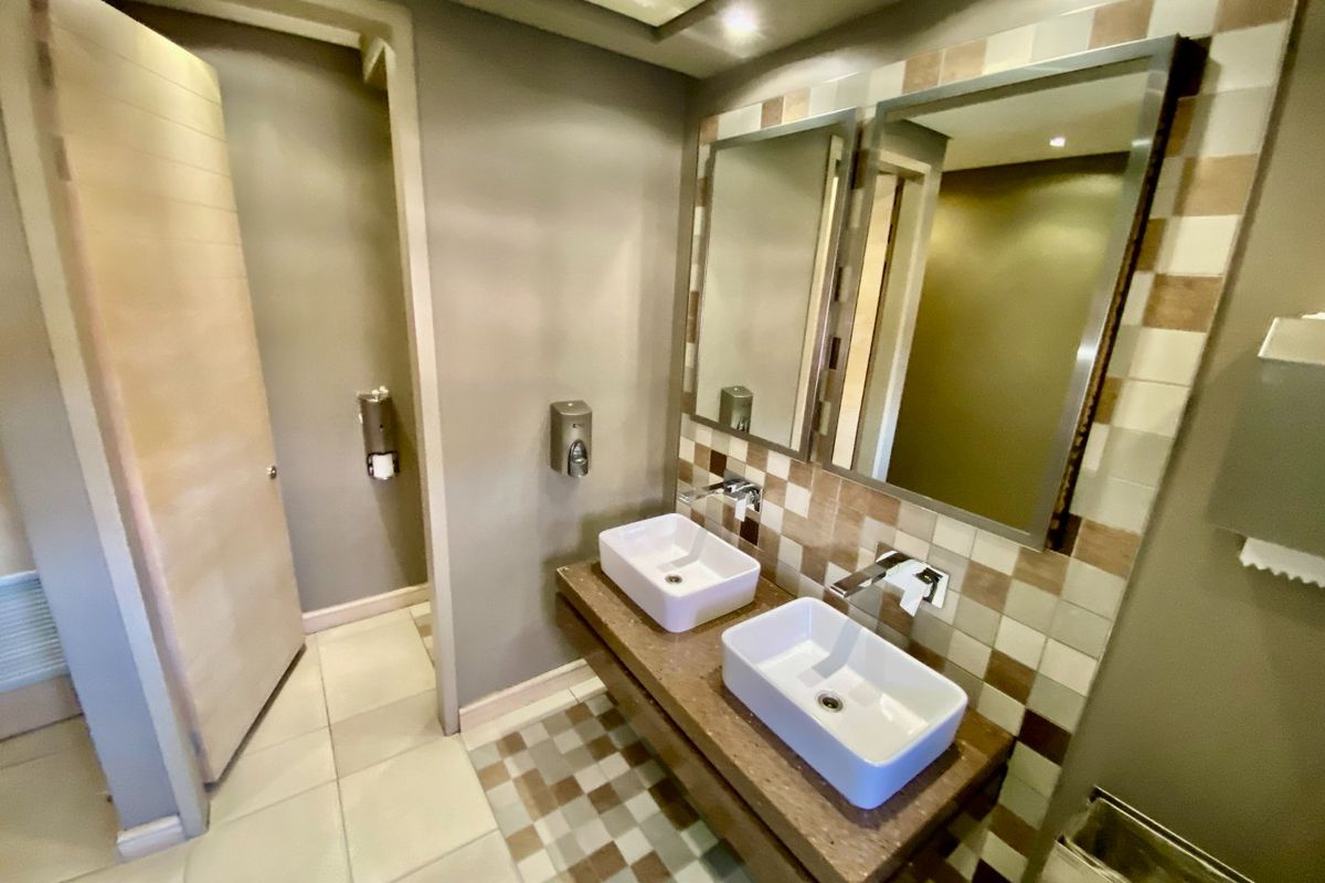 Modern commercial bathroom featuring a double vanity with vessel sinks, tiled backsplash, and wall-mounted soap dispensers.