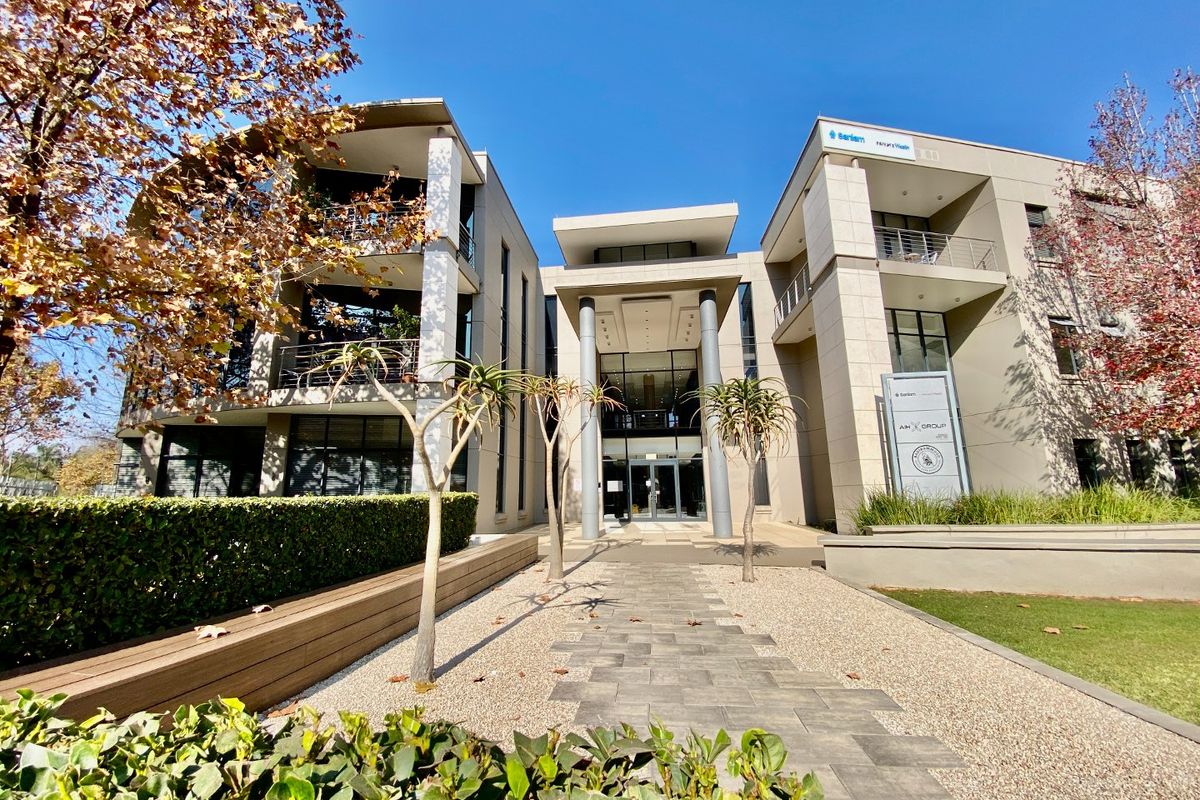 Modern commercial office building facade featuring a grand entrance, multi-level balconies, and professional landscaping with paved walkways.