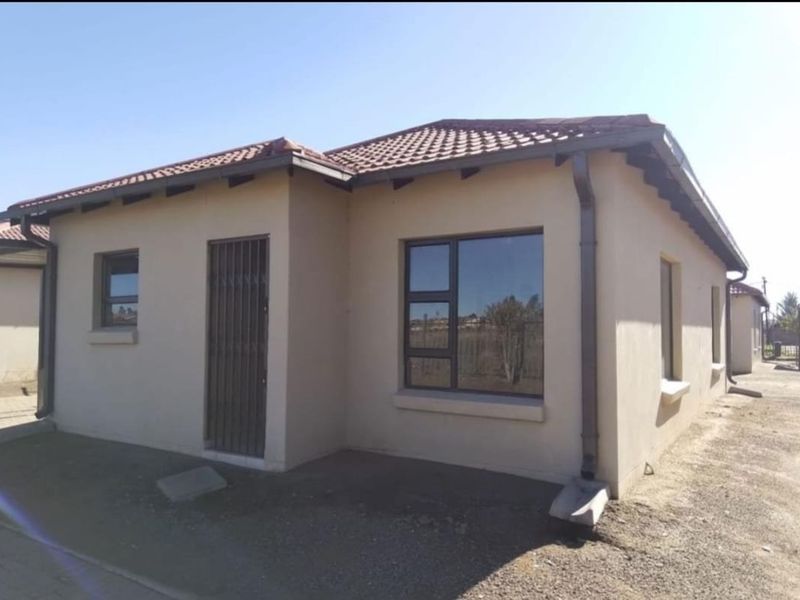 A view of the front exterior of a single-story house featuring plastered walls, a tiled roof, and aluminium window frames.