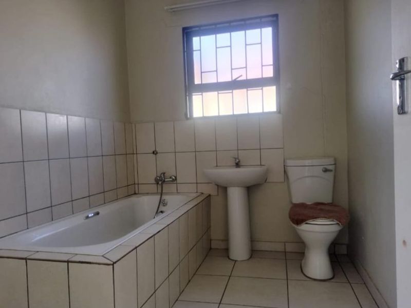 A functional bathroom featuring a built-in bathtub, pedestal basin, and toilet, finished with tiled flooring and wall splashbacks.