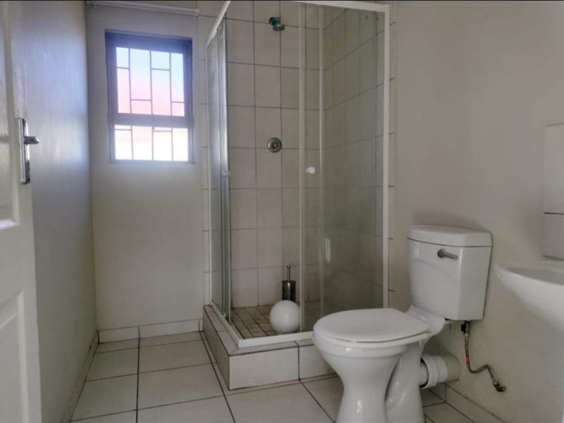 A functional bathroom featuring a glass shower enclosure, white toilet, and pedestal basin with tiled flooring and walls.