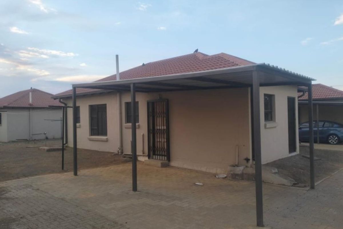 Rear view of the property featuring a covered carport area, paved driveway, and tiled roof structure.