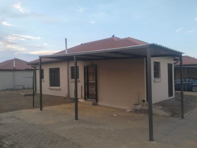 Rear view of the property featuring a covered carport area, paved driveway, and tiled roof structure.