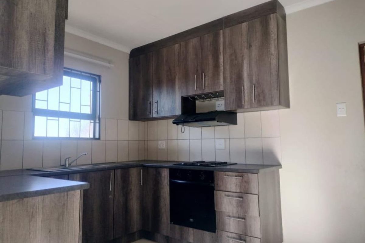 A clean, functional kitchen featuring dark wood-look cabinetry, built-in oven with gas hob, extractor fan, and tiled backsplash.