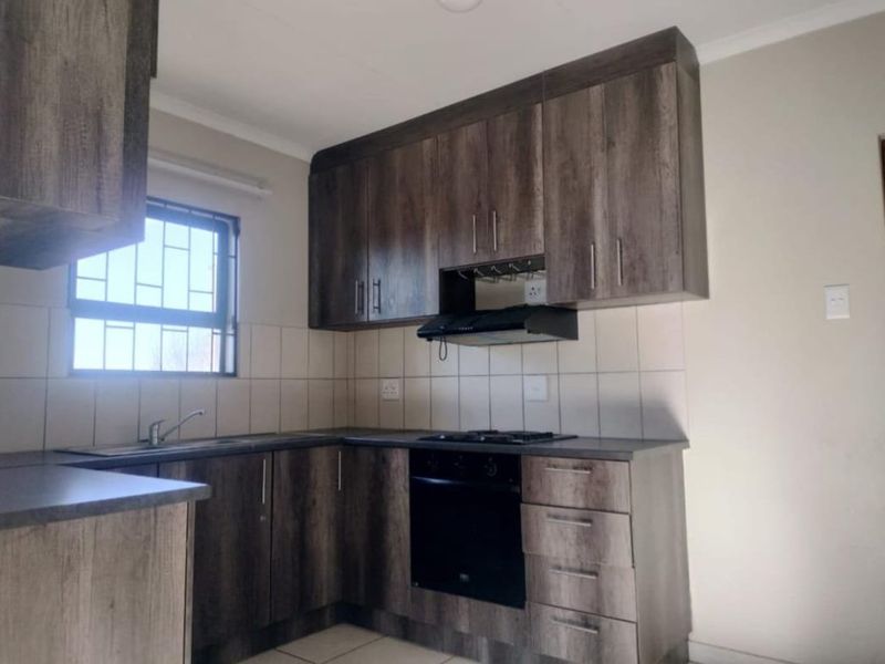 A clean, functional kitchen featuring dark wood-look cabinetry, built-in oven with gas hob, extractor fan, and tiled backsplash.