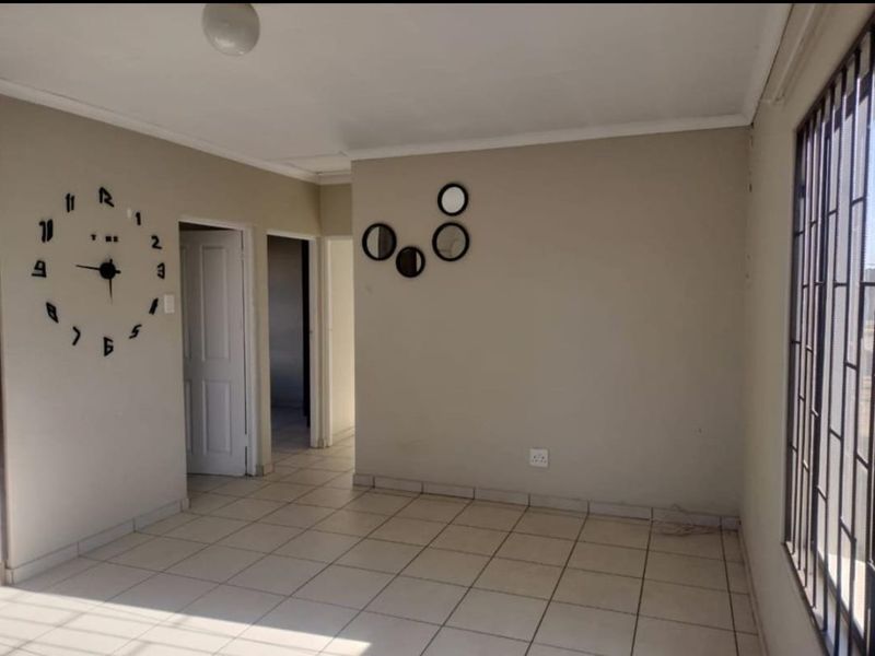 A bright, empty living area featuring neutral tiled flooring, coved ceilings, and security bars on the windows, offering a clean canvas for personalization.