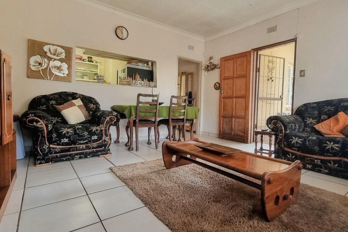 A living room featuring tiled flooring, a serving hatch connecting to the kitchen, and a wooden door leading to an exterior security gate.