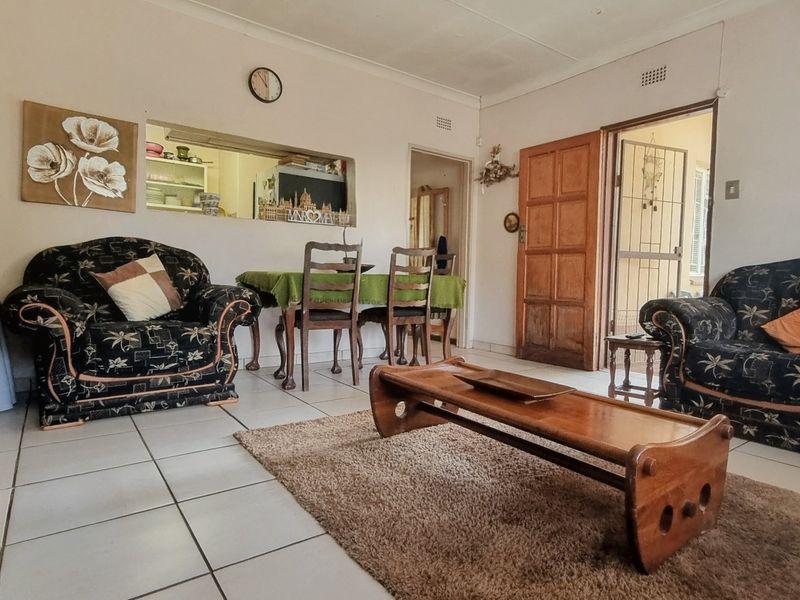 A living room featuring tiled flooring, a serving hatch connecting to the kitchen, and a wooden door leading to an exterior security gate.
