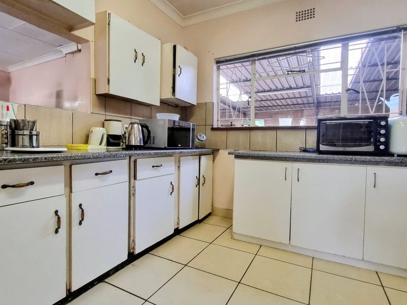 A functional kitchen featuring tiled flooring, laminate countertops, and original built-in cabinetry, offering potential for a modern renovation.